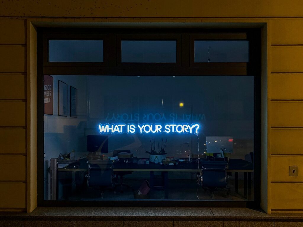 Neonskilt i butiksvindue med teksten "What Is Your Story?" i blåt lys